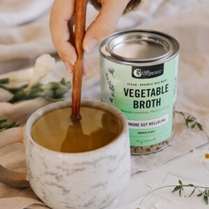 Nutra Organics Vegetable Broth in a styled image with fresh hot cup of both along side of product container