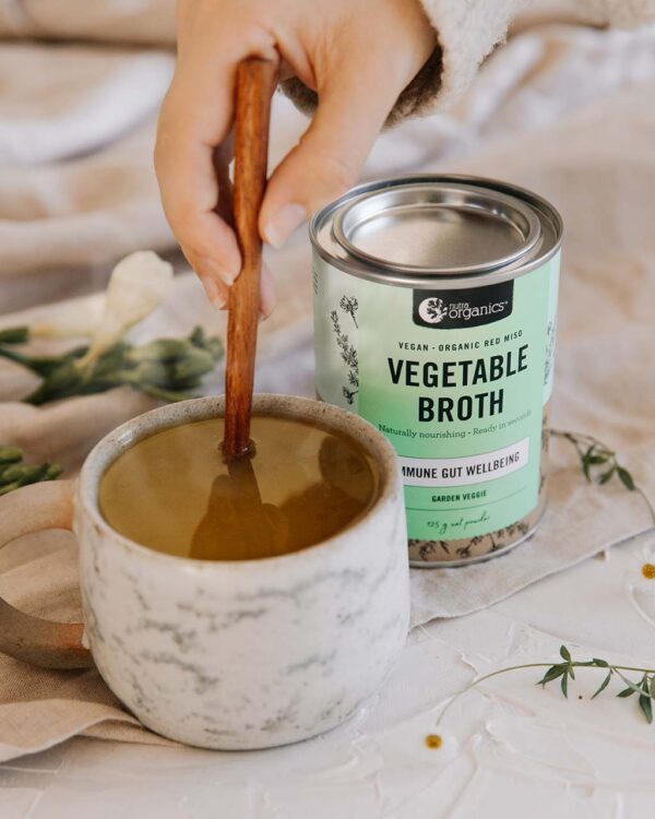 Nutra Organics Vegetable Broth in a styled image with fresh hot cup of both along side of product container