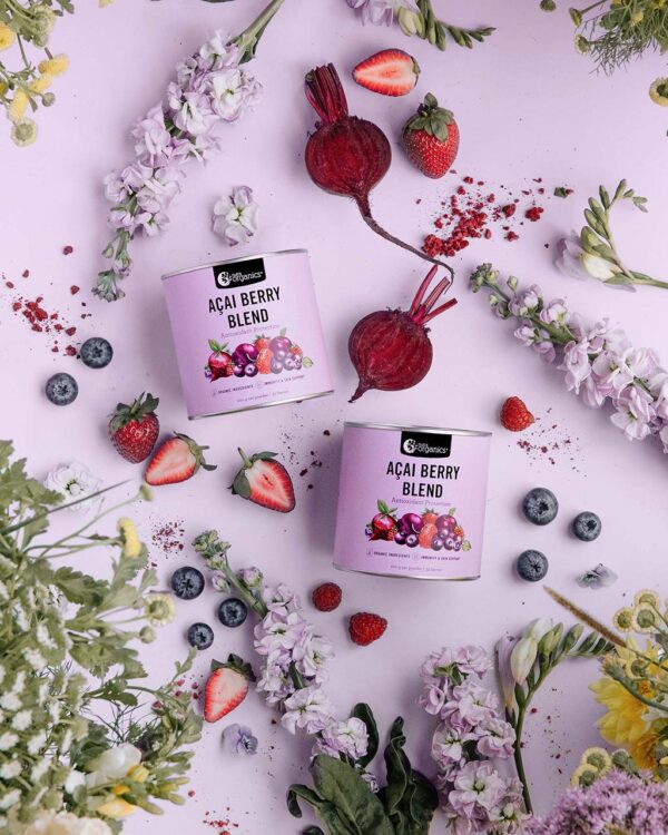 Nutra Organics Acai Berry Blend in a styled image with 2 containers of product displayed with strawberries, beets, blueberries, and flowers